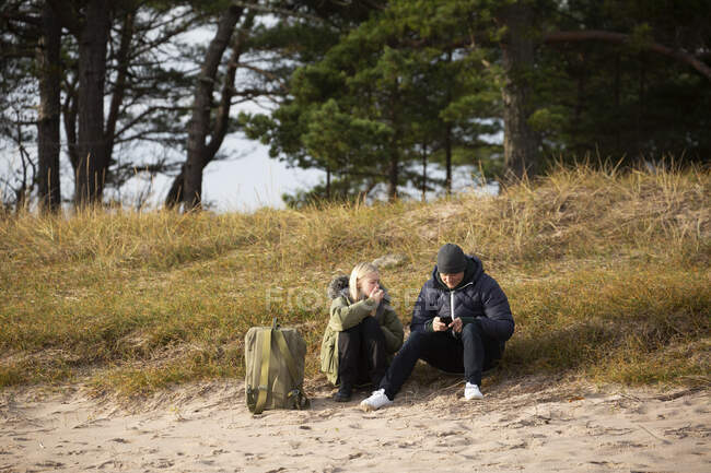 Padre e hija sentados en la hierba por la playa - foto de stock