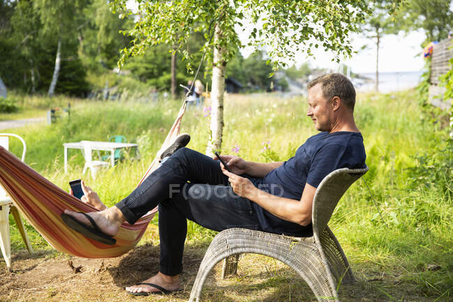 Человек, использующий смартфон, сидя в плетеном кресле — стоковое фото