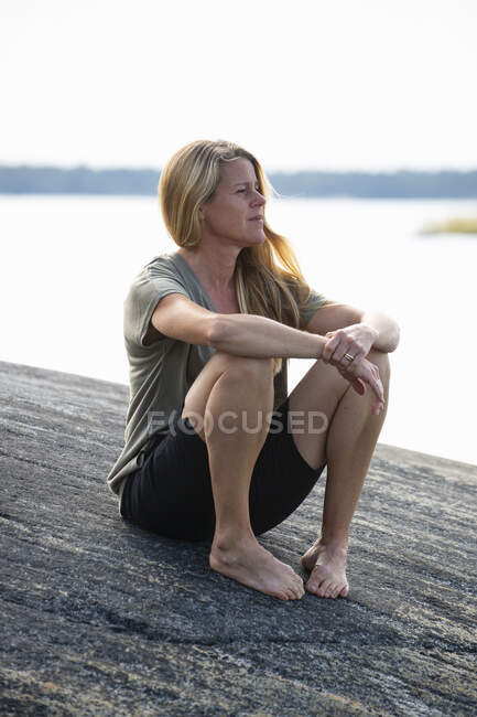 Femme assise sur le rocher par la mer — Photo de stock