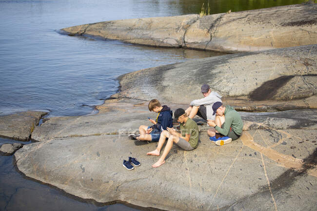 Teenage boys sitting on rock by sea — Fotografia de Stock