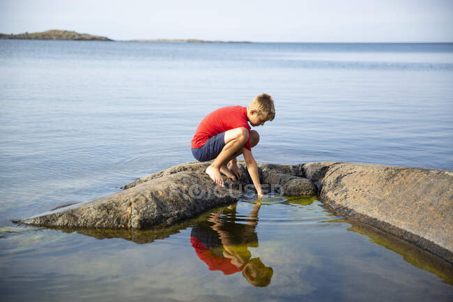 Boy crouching on rock in sea — Stock Photo