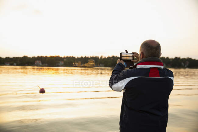 Homme photographiant lac au coucher du soleil — Photo de stock