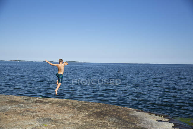Хлопчик занурюється зі скелі в море — стокове фото