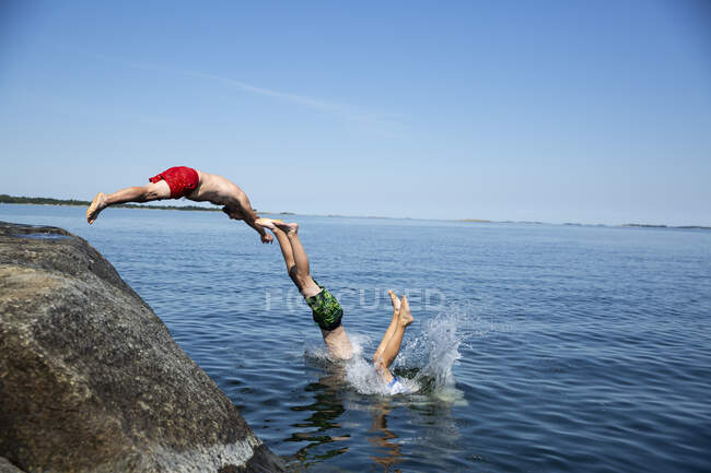 Father and sons diving from rock into sea — Fotografia de Stock