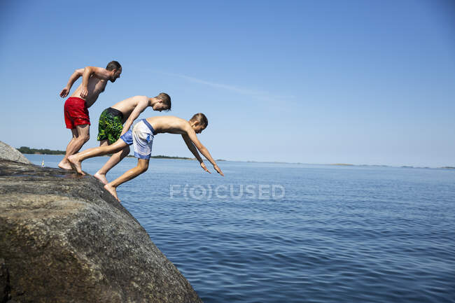 Padre e hijos buceando desde la roca en el mar - foto de stock