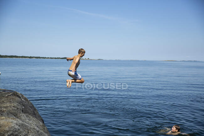 Chico buceando desde la roca hasta el mar - foto de stock