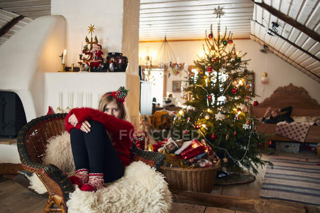 Girl sitting on armchair by Christmas tree — Fotografia de Stock