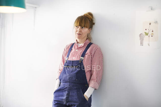 Artist wearing overalls leaning on wall by painting — Stock Photo