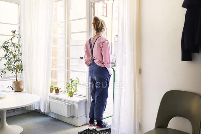 Mulher vestindo macacão e camisa listrada pela janela — Fotografia de Stock