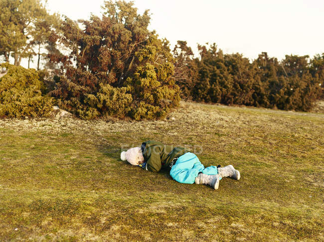 Menina vestindo roupas quentes deitado na grama por árvores — Fotografia de Stock