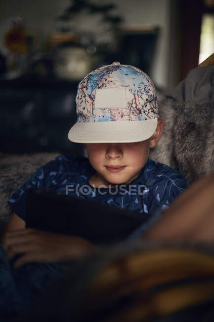 Niño en gorra de colores sentado en el sofá - foto de stock