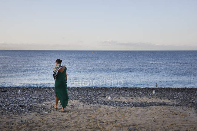 Mujer joven en vestido verde caminando en la playa - foto de stock