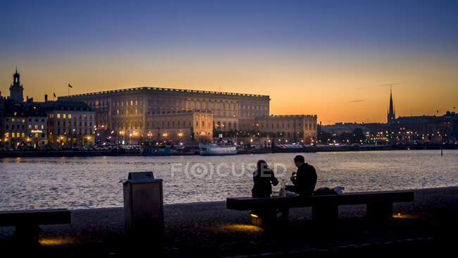 Pareja sentada junto al puerto de Estocolmo, Suecia al atardecer - foto de stock