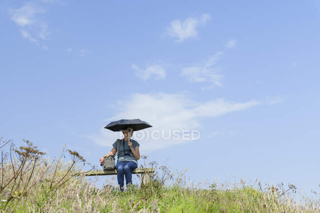 Donna anziana con ombrello seduta su panchina in collina — Foto stock