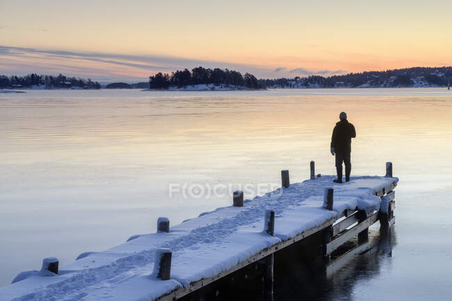 Man on snowy jetty on lake at sunset — Stock Photo