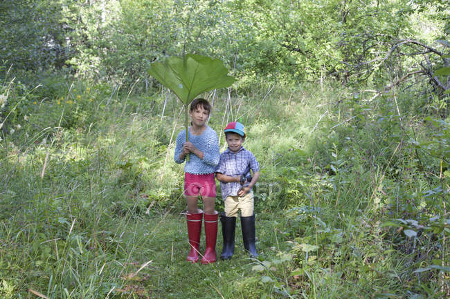 Menino e menina com folha grande na floresta — Fotografia de Stock