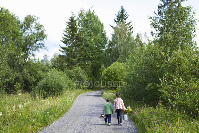 Siblings with flowers walking on road — Stock Photo