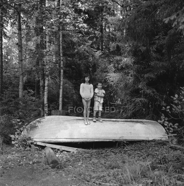 Дети, стоящие на опрокинутой лодке в лесу — стоковое фото