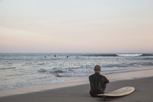 Uomo con tavola da surf seduto sulla spiaggia — Foto stock