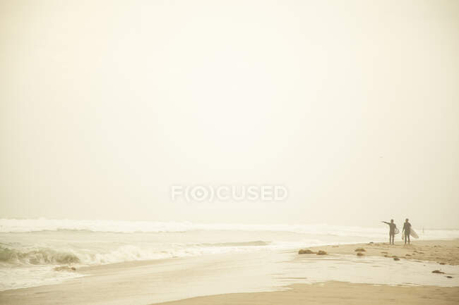 Surfistas caminando en la playa al atardecer - foto de stock