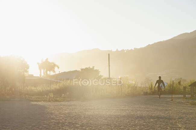 Homem transportando prancha ao pôr do sol — Fotografia de Stock