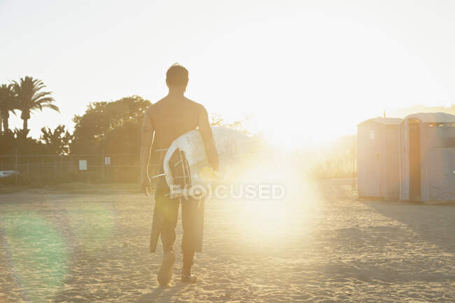 Hombre llevando tabla de surf al atardecer - foto de stock