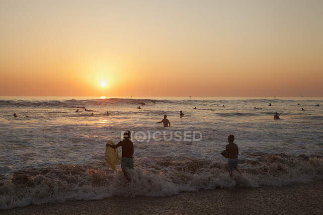 Люди плавають у морі під час заходу сонця. — стокове фото