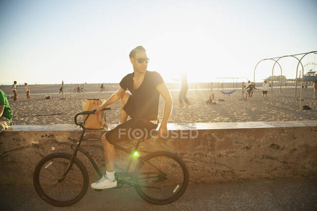 Людина з велосипедом під сонцем на пляжі. — стокове фото