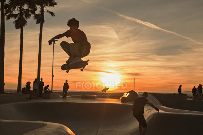 Мальчик-подросток катается в скейтпарке на закате — стоковое фото