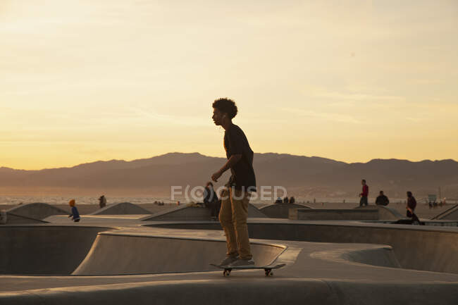 Мальчик-подросток катается в скейтпарке на закате — стоковое фото