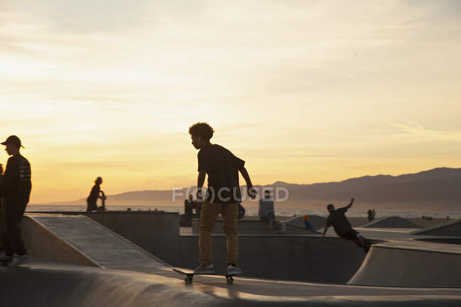 Jeune garçon patinant au skatepark pendant le coucher du soleil — Photo de stock