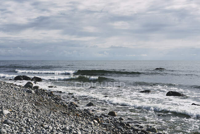 Облака над волнами на каменном пляже — стоковое фото