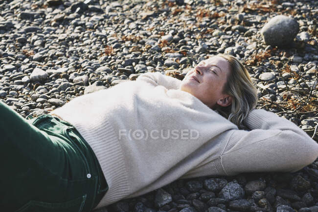 Mujer en suéter acostada en la orilla del río - foto de stock