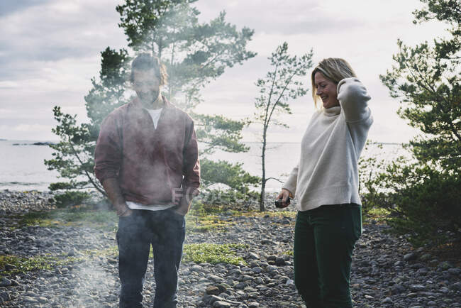 Hombre y mujer sonrientes en humo de fogata - foto de stock