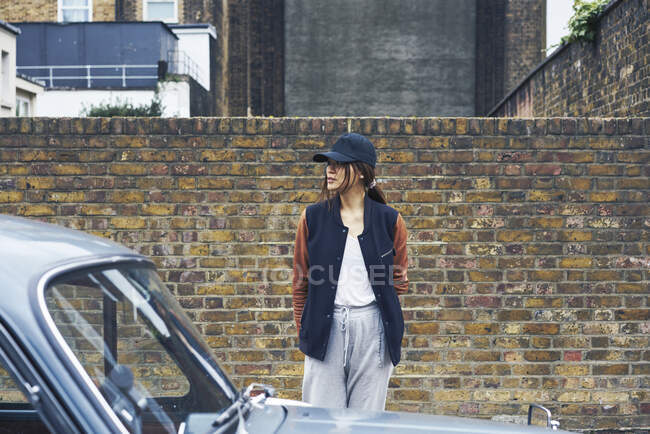 Mujer de pie en la calle por la pared de ladrillo y coche - foto de stock