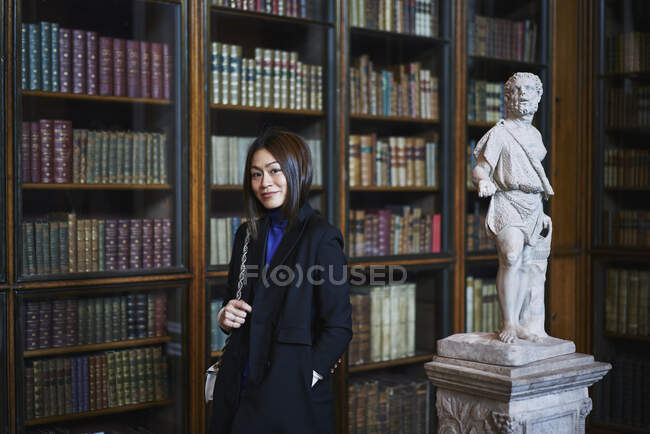 Retrato de mulher por escultura em biblioteca — Fotografia de Stock