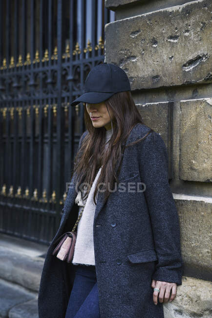 Mulher de chapéu e casaco apoiada na parede — Fotografia de Stock