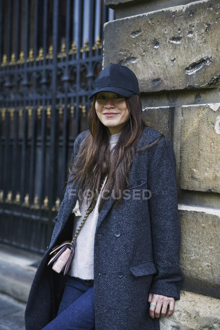Mulher de chapéu e casaco apoiada na parede — Fotografia de Stock