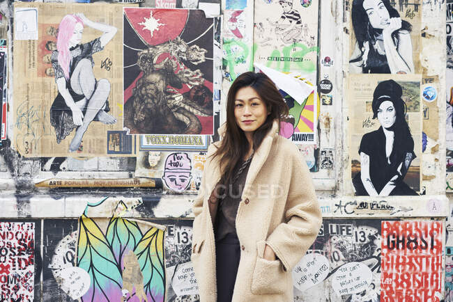 Жінка в пальто біля стіни з вуличним мистецтвом — стокове фото