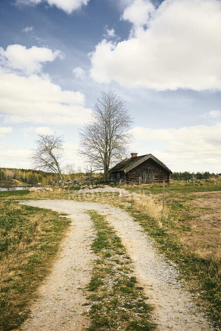 Rural road and cabin below clouds — Stock Photo