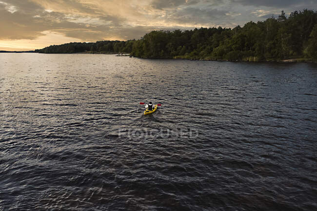 Homem de caiaque no lago durante o pôr do sol — Fotografia de Stock