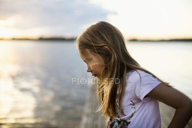 Menina por lago durante o pôr do sol — Fotografia de Stock