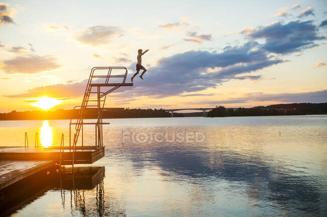 Garçon plongeant dans le lac au coucher du soleil — Photo de stock
