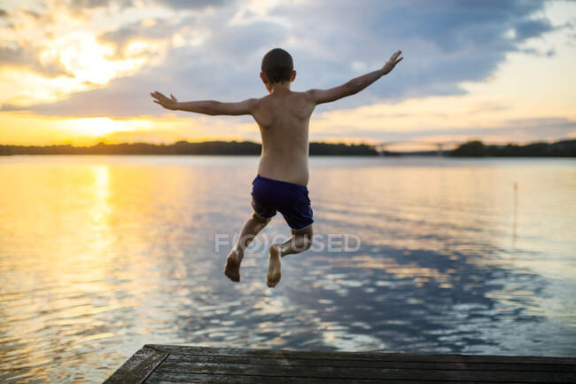 Хлопчик занурюється в озеро на заході сонця — стокове фото
