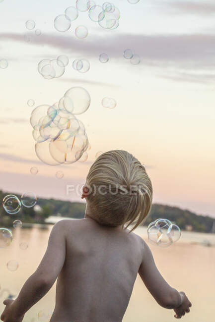 Garçon jouer avec des bulles au coucher du soleil — Photo de stock