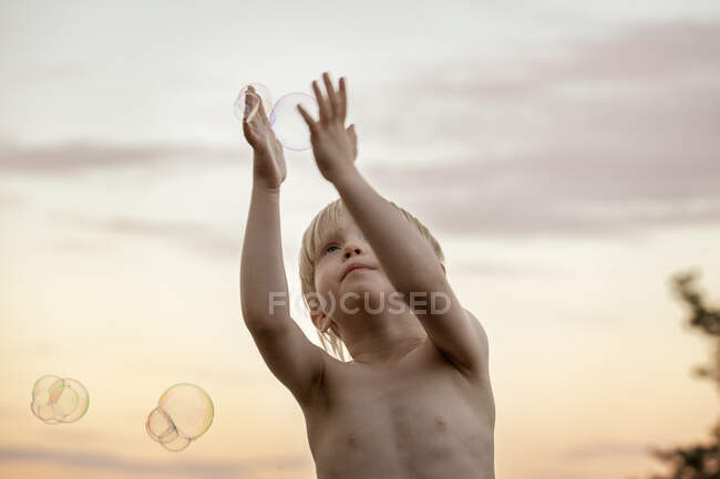 Garçon jouer avec des bulles au coucher du soleil — Photo de stock