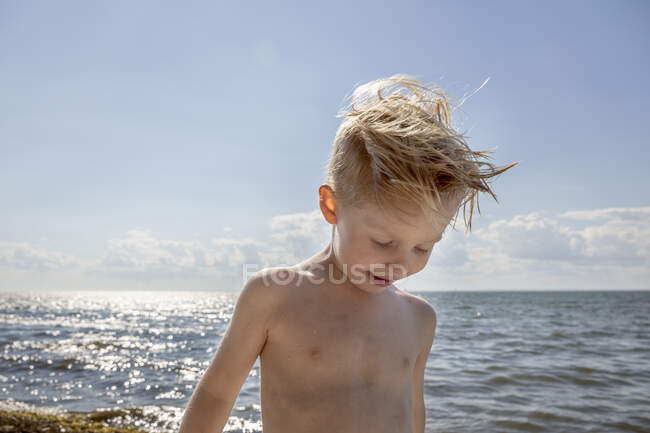 Hemdloser Junge unter Wolken am Strand — Stockfoto