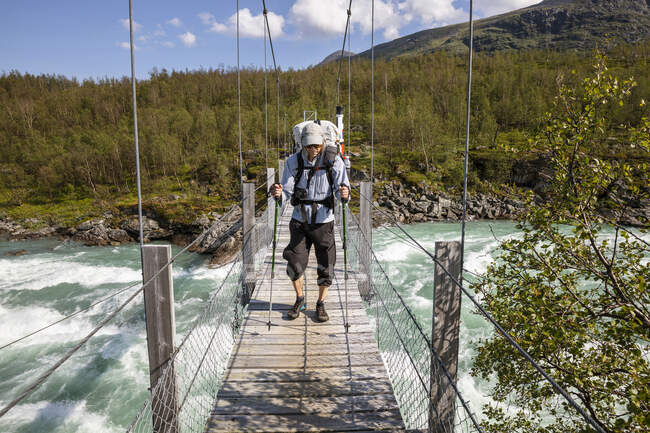 Homme randonnée sur pont sur rivière — Photo de stock