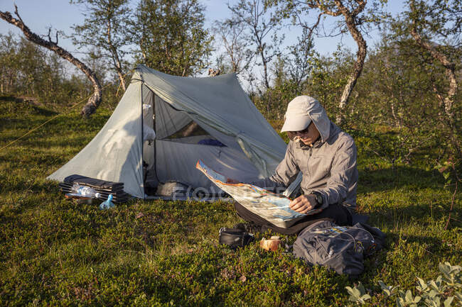 Hombre leyendo en el mapa mientras acampa - foto de stock