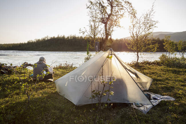 Homem acampar com barraca por rio — Fotografia de Stock